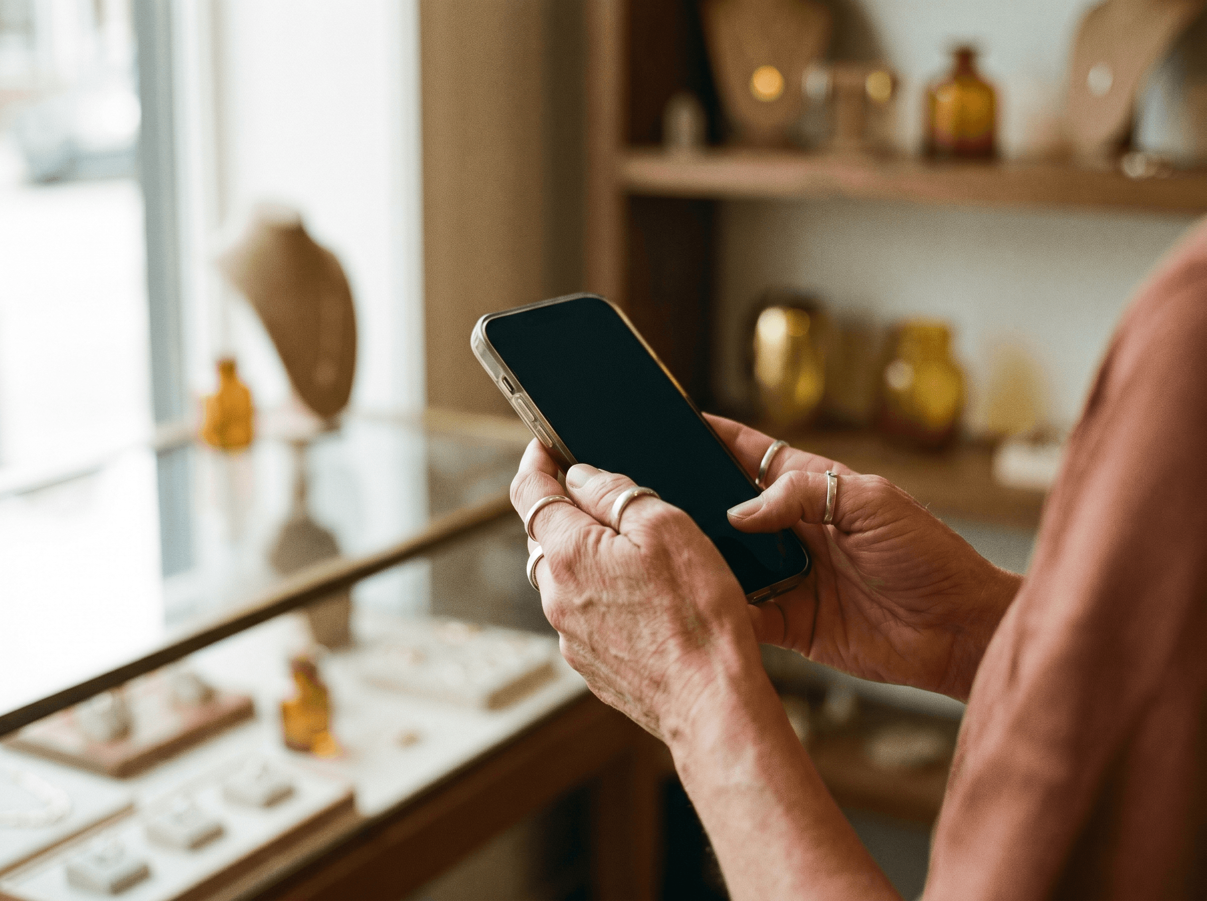 Hands holding a smartphone in front of a jewelry display case in a boutique