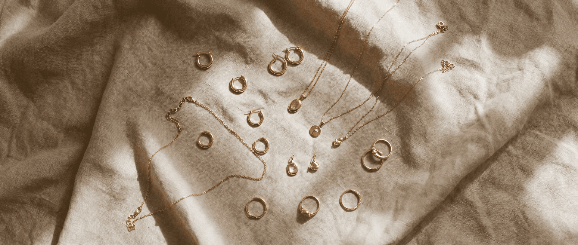 Overhead flat-lay of gold jewelry arranged on a warm linen surface