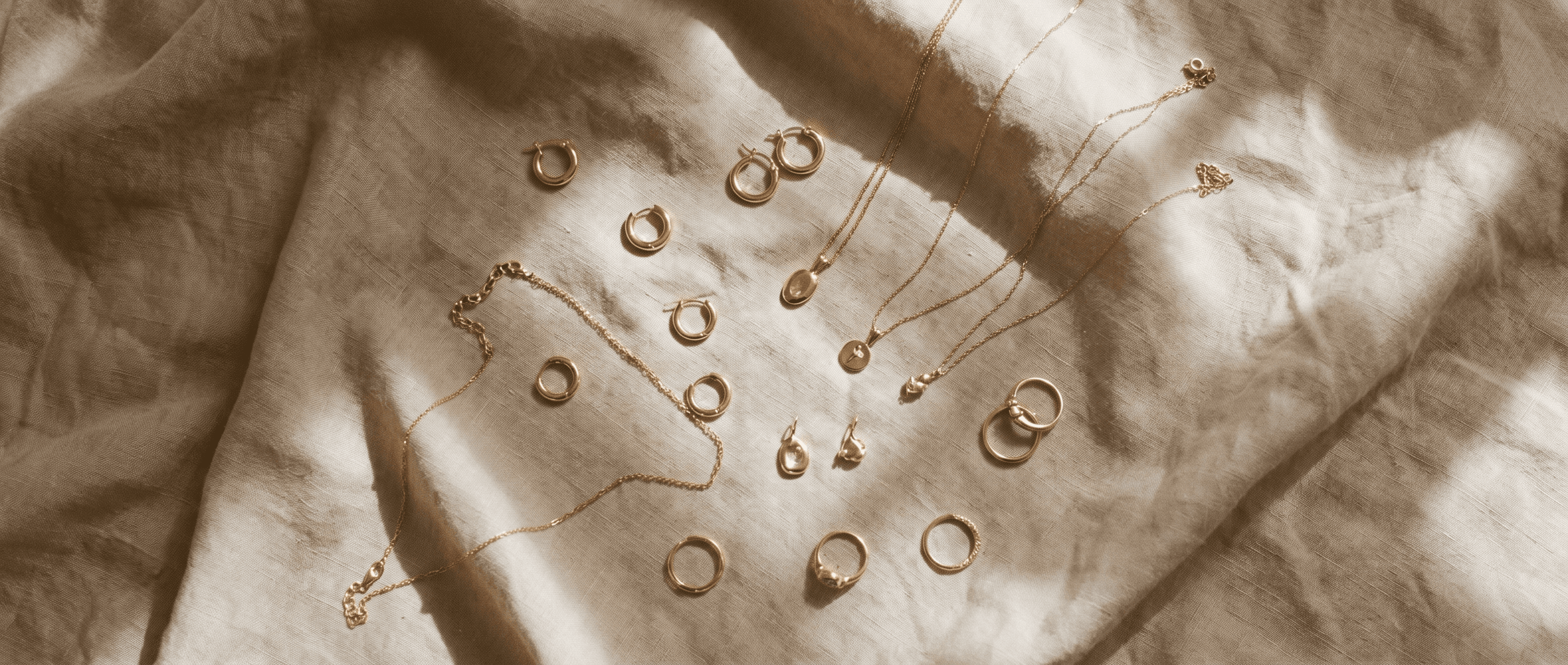 Overhead flat-lay of gold jewelry arranged on a warm linen surface