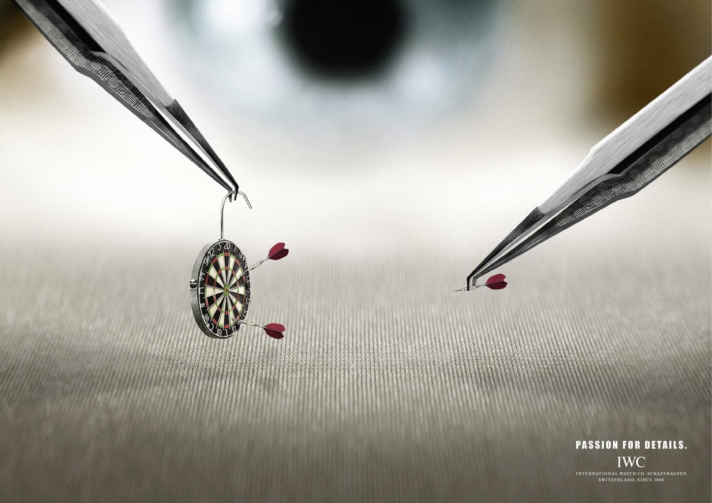 IWC Watchmaker Darts ad showing tweezers holding a miniature dartboard, Passion for Details campaign