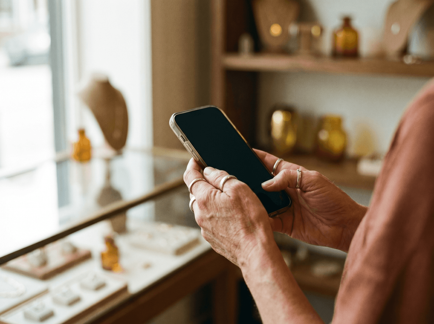 Hands holding a smartphone in front of a jewelry display case in a boutique