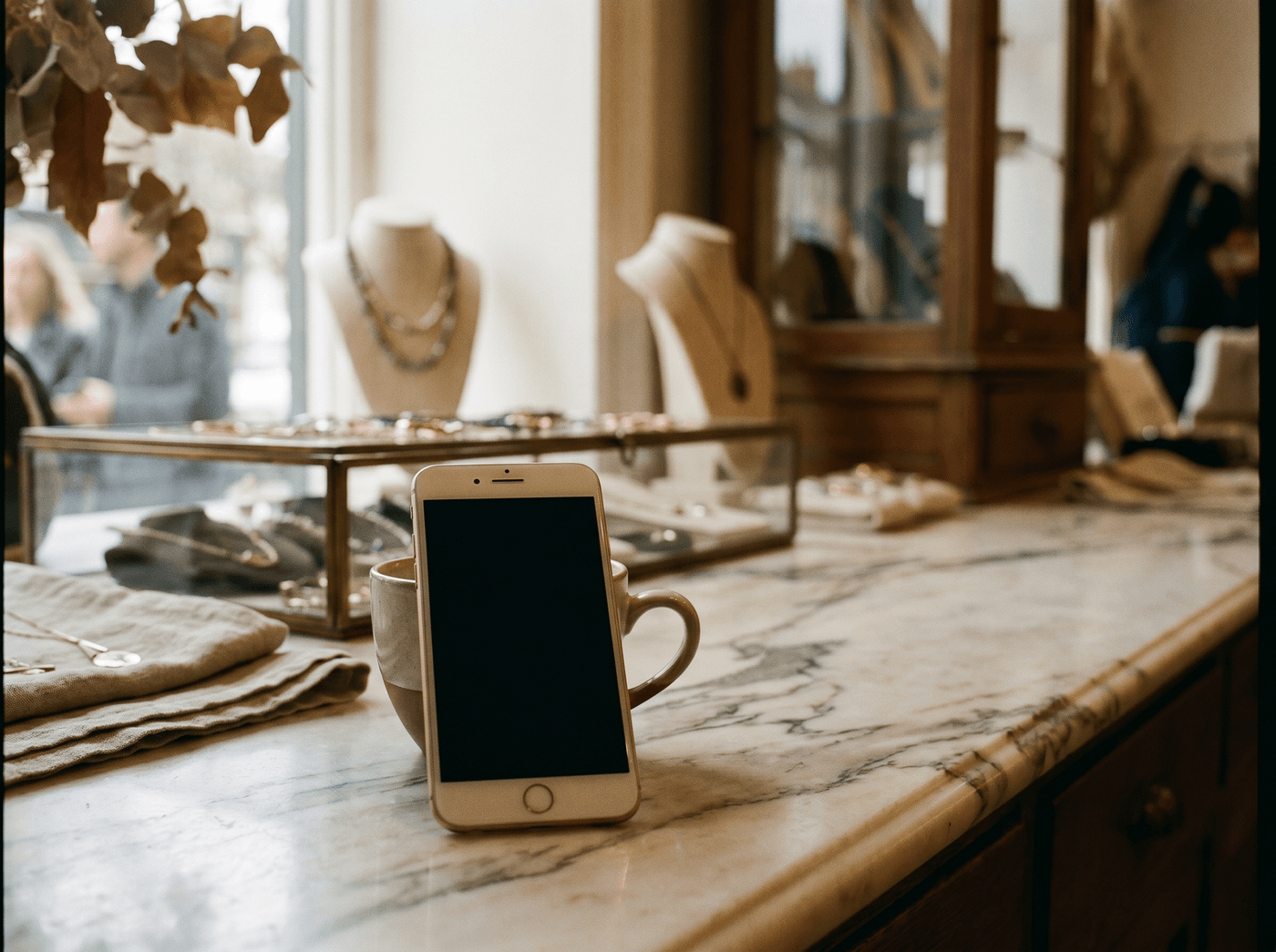 A smartphone leaning against a coffee cup on a marble counter in a jewelry boutique at morning