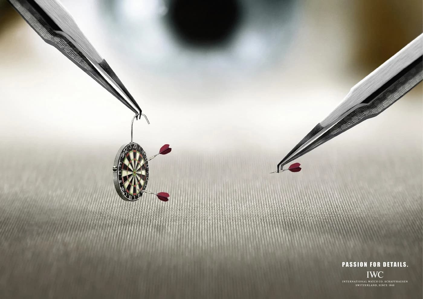 IWC Watchmaker Darts ad showing tweezers holding a miniature dartboard, Passion for Details campaign
