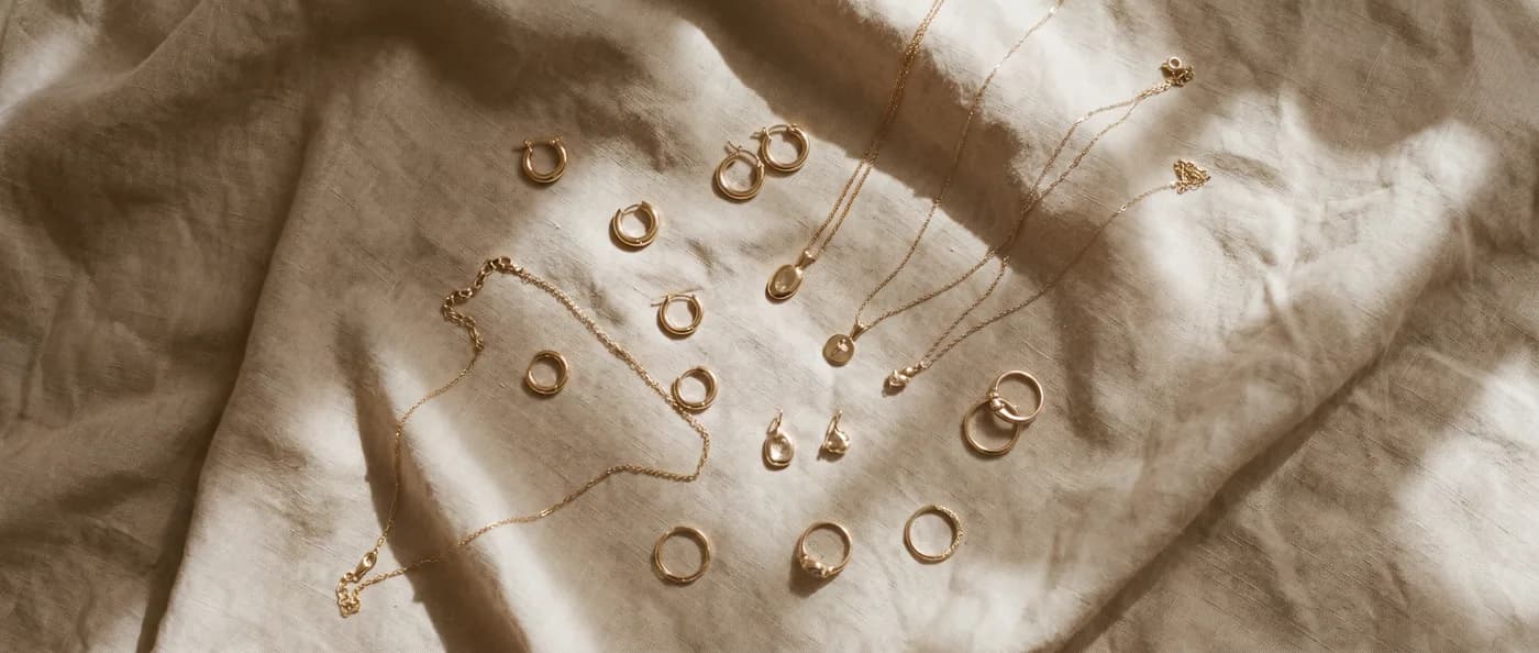Overhead flat-lay of gold jewelry arranged on a warm linen surface