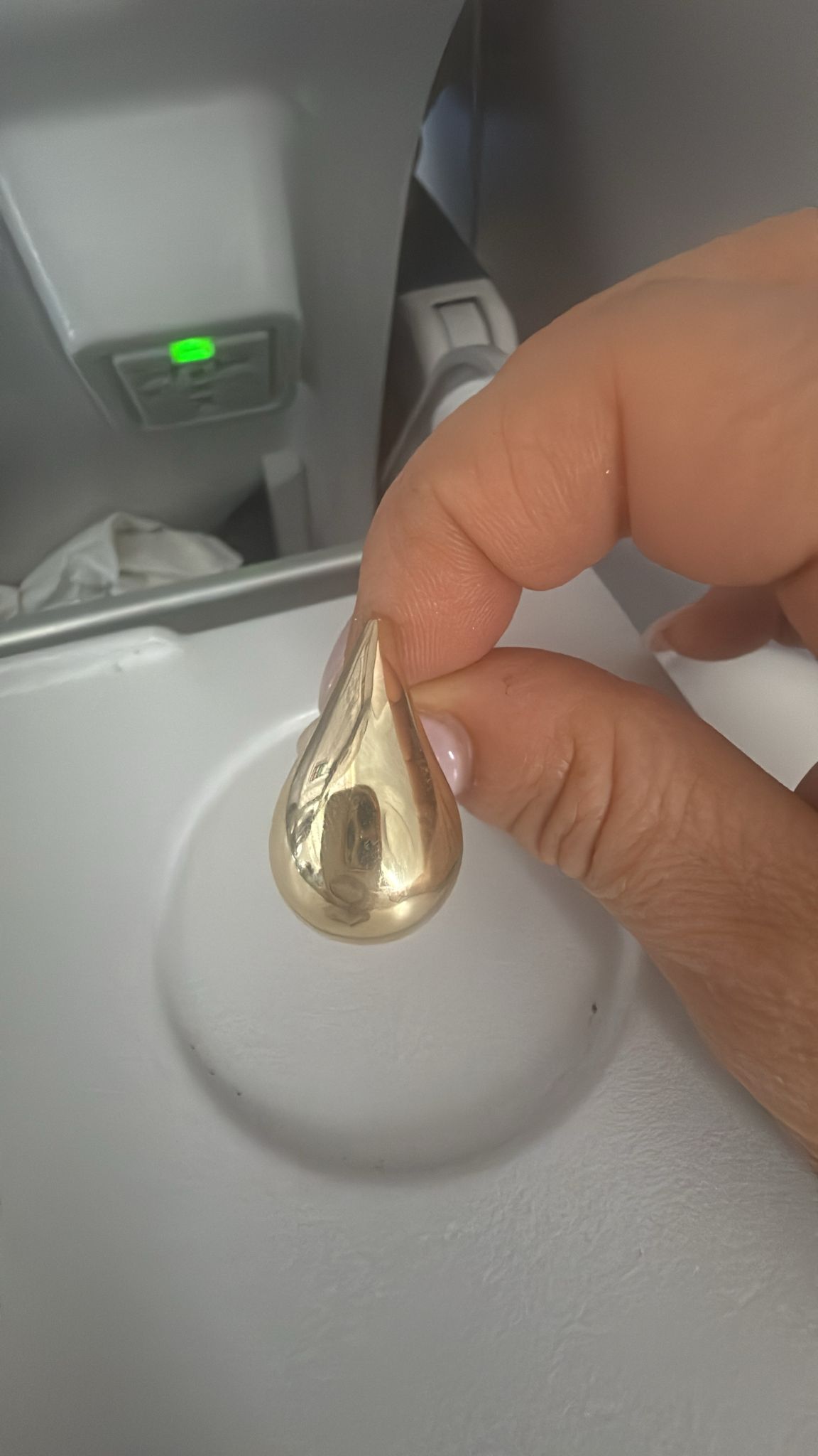 A gold teardrop earring photographed on a phone