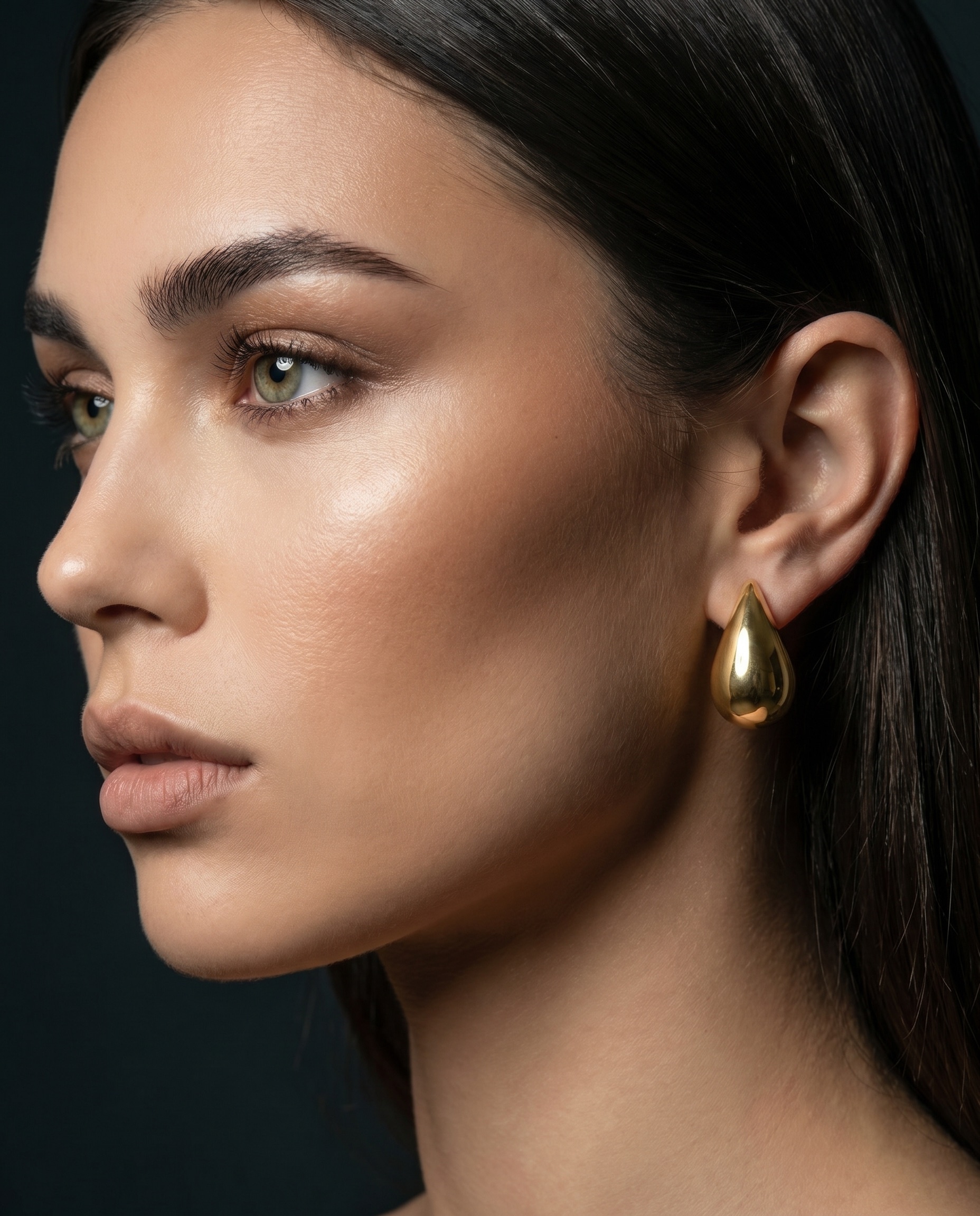 Model wearing a gold teardrop earring, shown to scale